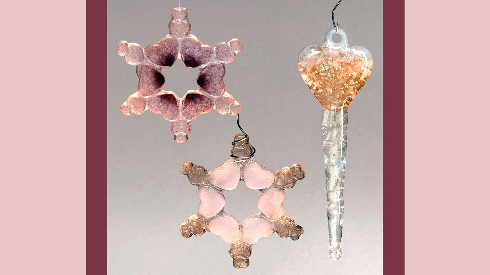 Three ornaments of fused glass in front of a grey background. Two are shaped like snowflakes made of small hearts, and the third is a heart with a long icicle below it.